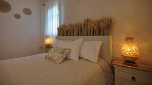 A bedroom with a bed, two bedside lamps, a nightstand, and a window with curtains. - Likavgies Comfort Maisonettes (Alonissos)