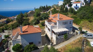A coastal residential area with houses featuring red-tiled roofs and white walls, surrounded by greenery and overlooking the sea. - Likavgies Comfort Maisonettes (Alonissos)