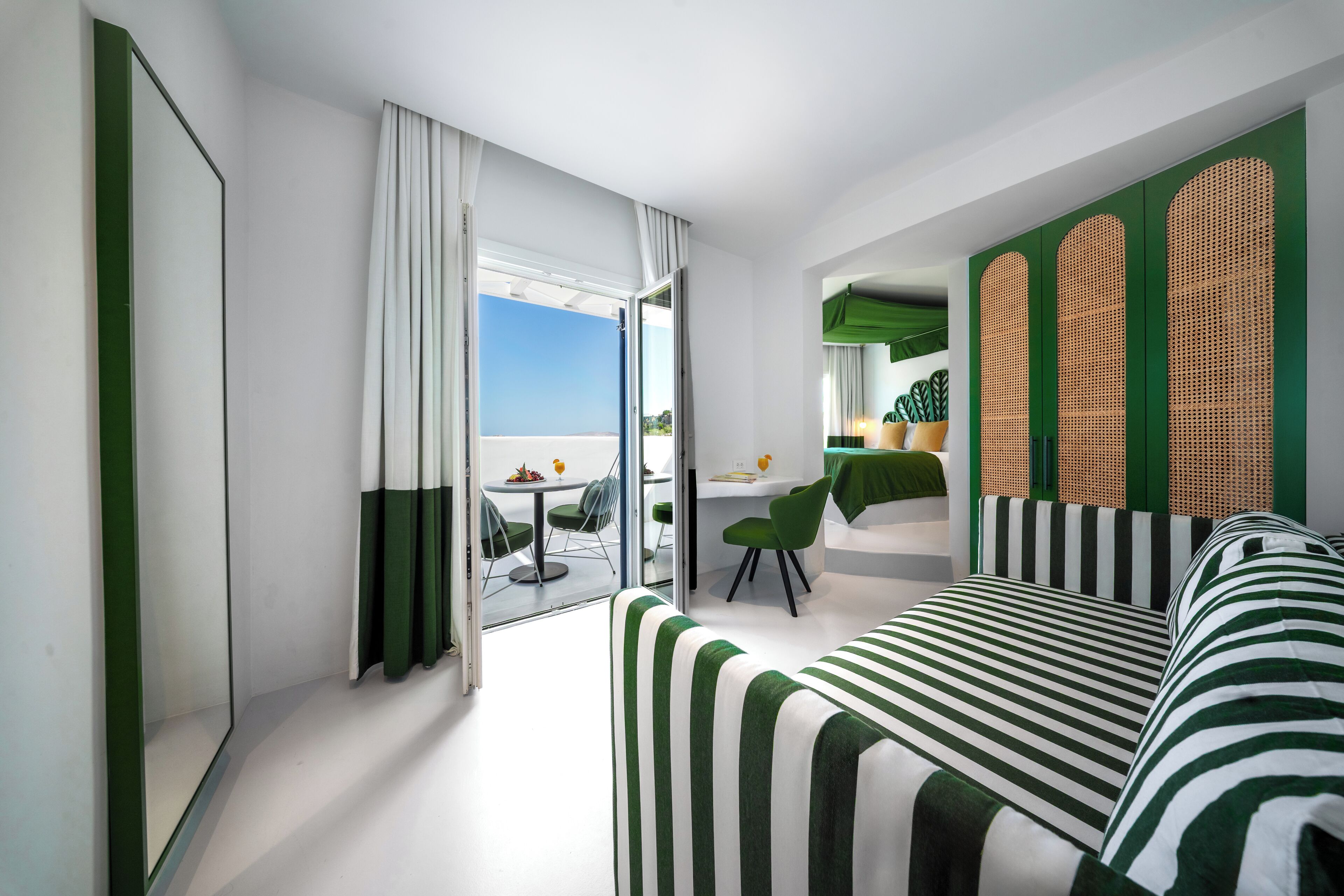 Habitación de hotel moderna con un sofá a rayas, un área de comedor con mesa y sillas, y vistas al exterior.