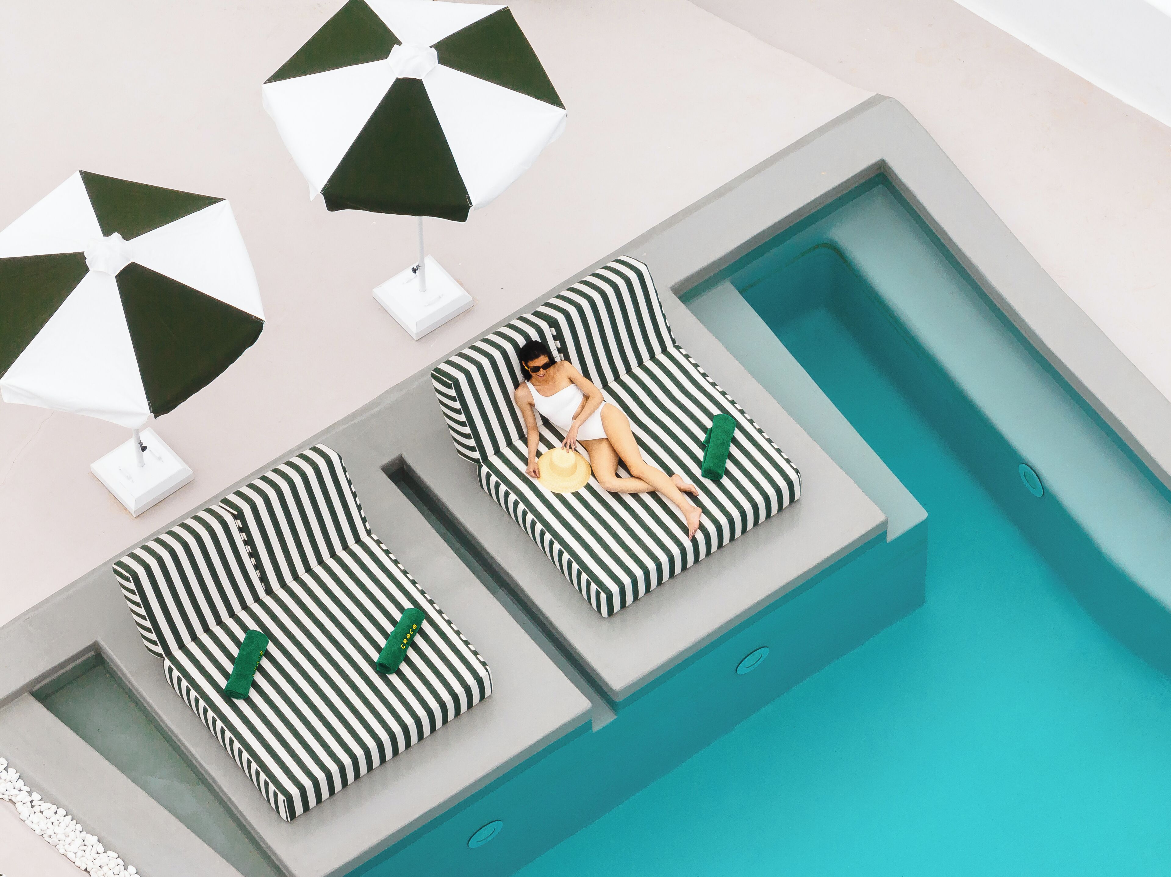 Zona de piscina con dos sillones de descanso y dos sombrillas.