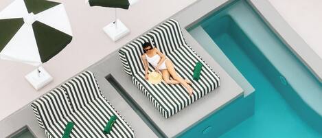 Zona de piscina con dos sillones de descanso y dos sombrillas.