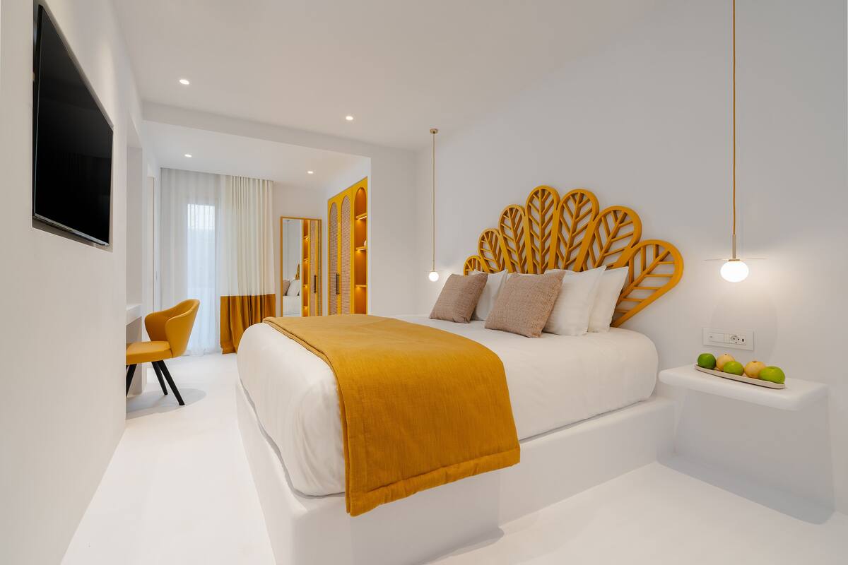 A modern bedroom with a large bed, a TV mounted on the wall, and a bedside table with fruit.