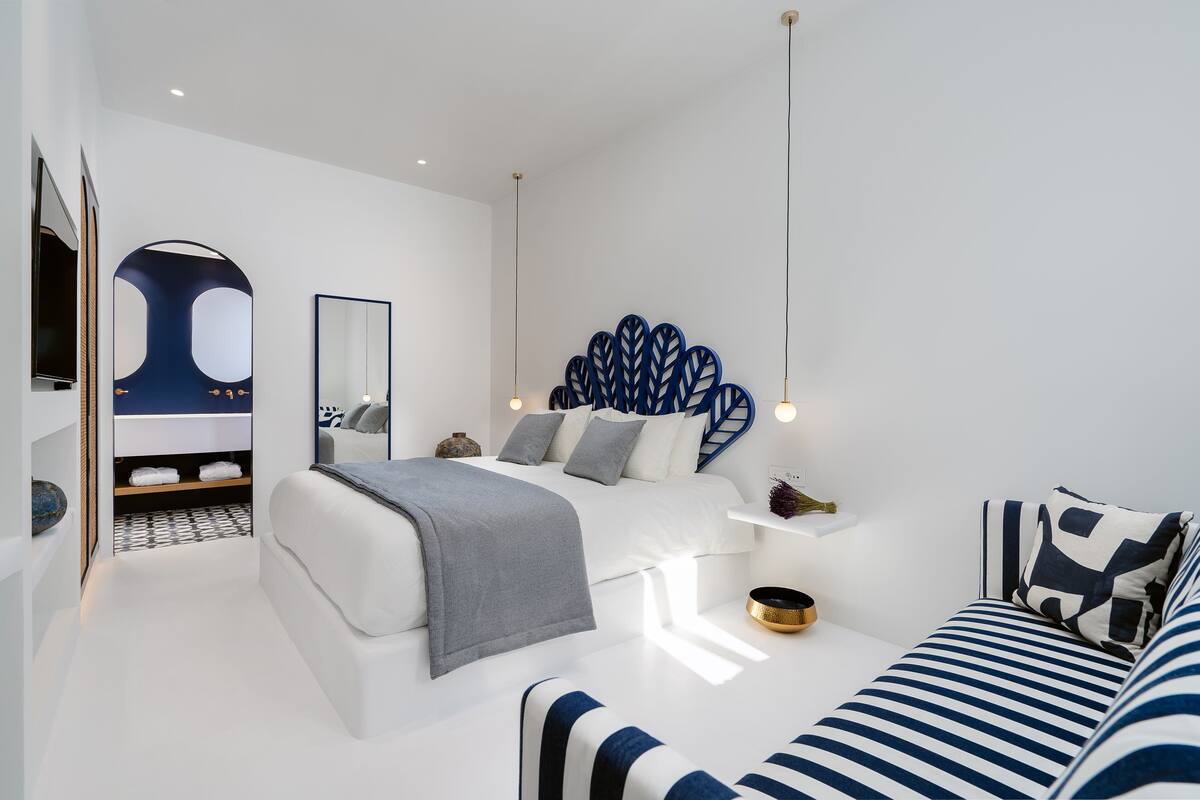 A modern bedroom with a bed, a sofa, a mirror, and a decorative wall piece.