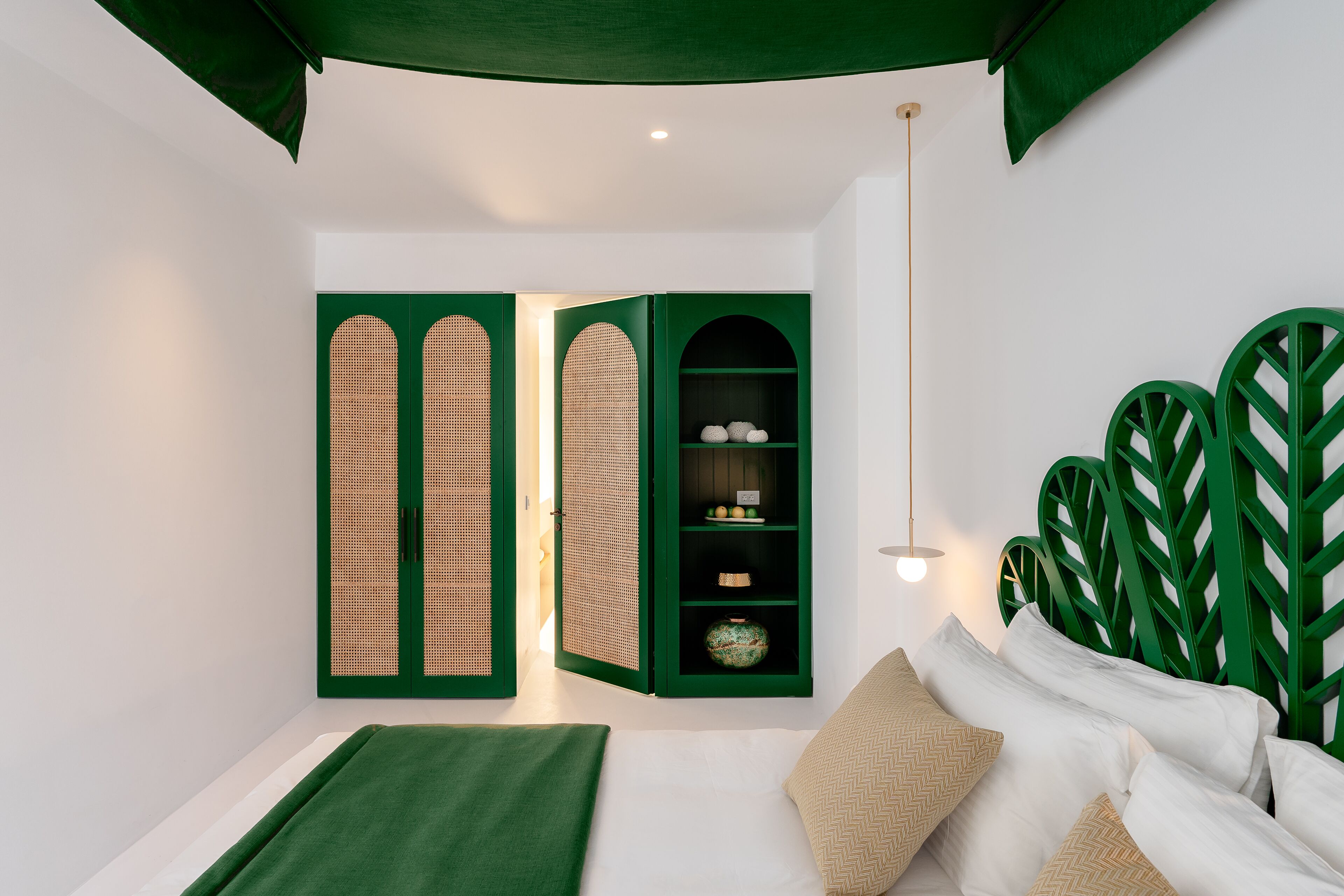 Un dormitorio con una cama, cabecera verde y un armario verde con estantes.