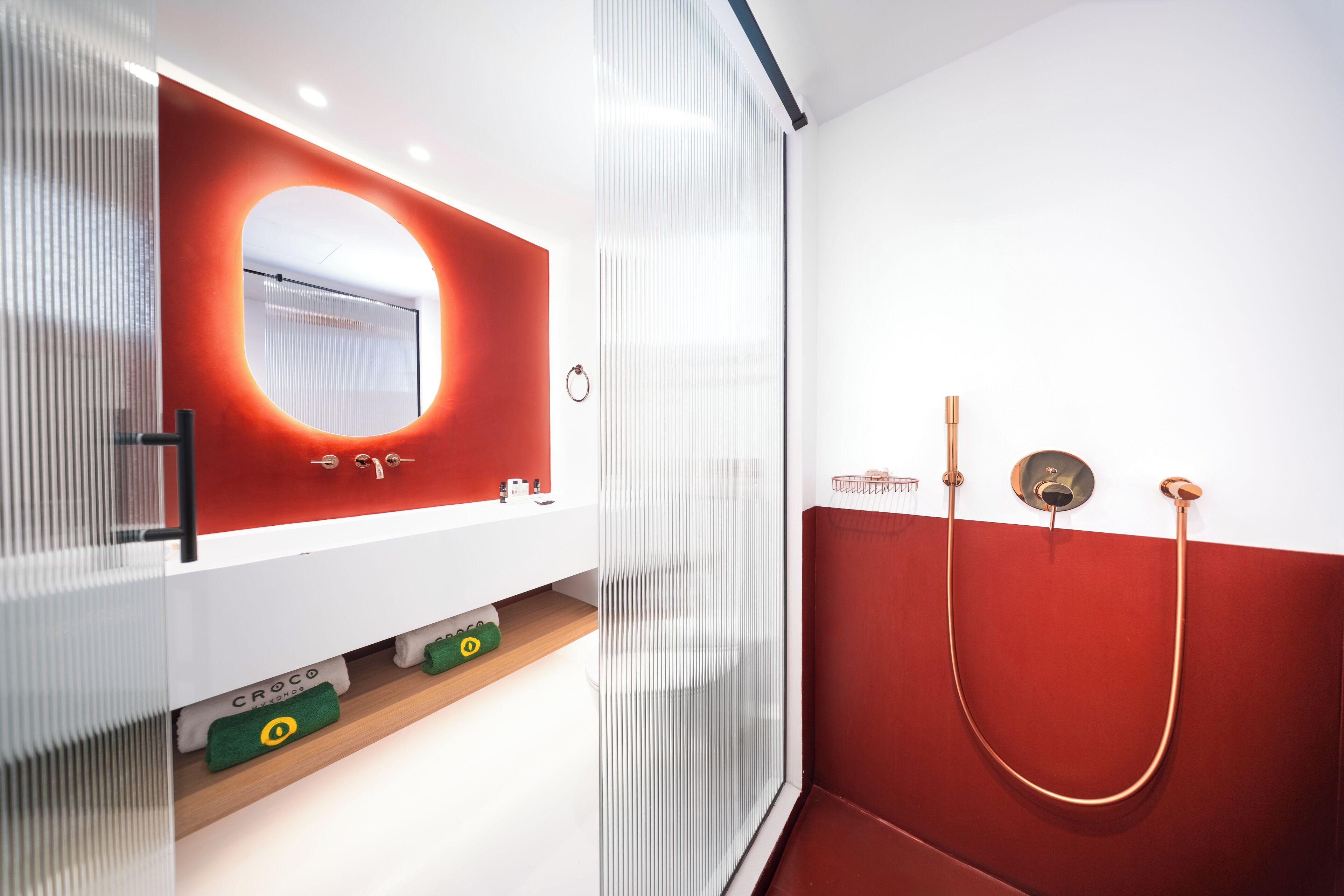 A modern bathroom with a white vanity, a red accent wall, and a glass shower enclosure.