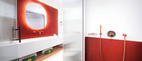 A modern bathroom with a white vanity, a red accent wall, and a glass shower enclosure.