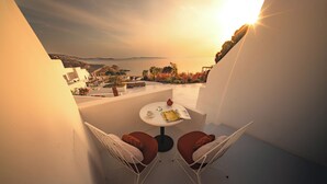 A balcony with two white chairs, a small round table, and a view of the sea at sunset. - Croco Mykonos (Mykonos)