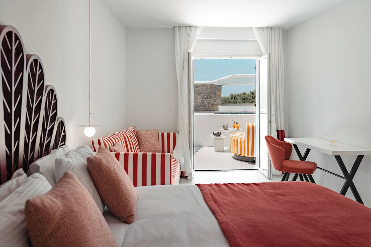 A modern hotel room with a bed, a desk, a chair, and a balcony with a view.