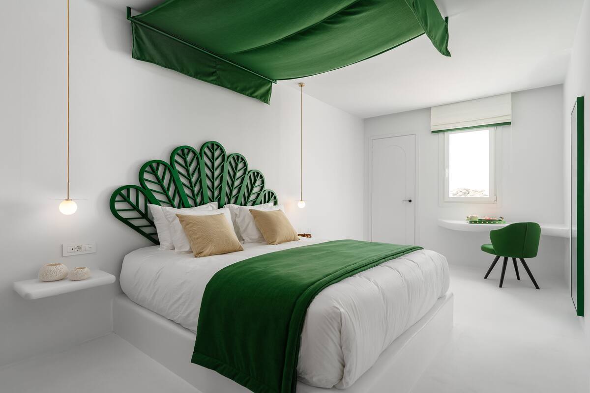 A modern bedroom with a large bed, a green canopy, a small desk, and a chair.