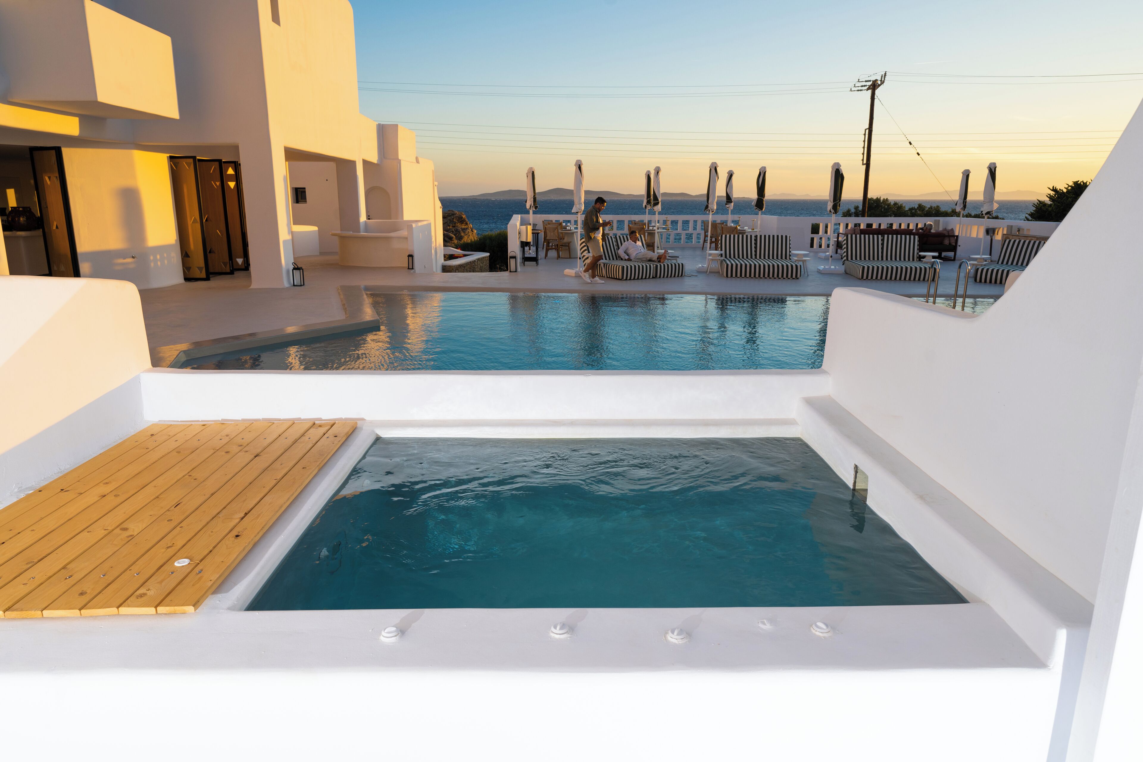 A rooftop pool area with a hot tub, lounge chairs, and a view of the sea.