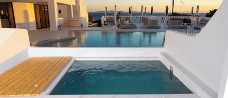 A rooftop pool area with a hot tub, lounge chairs, and a view of the sea.