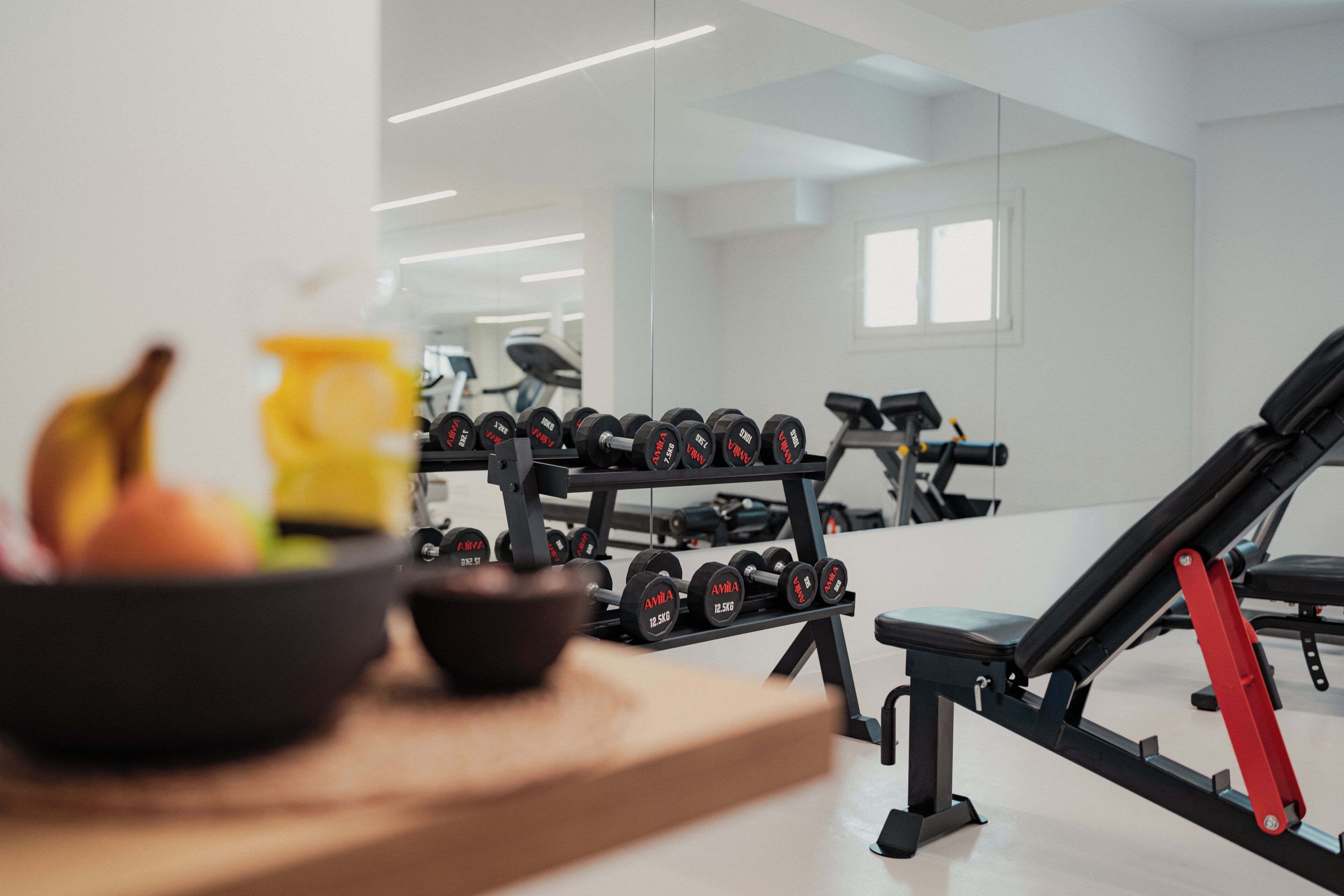 A gym with exercise equipment, a bench, and a bowl of fruit on a table.