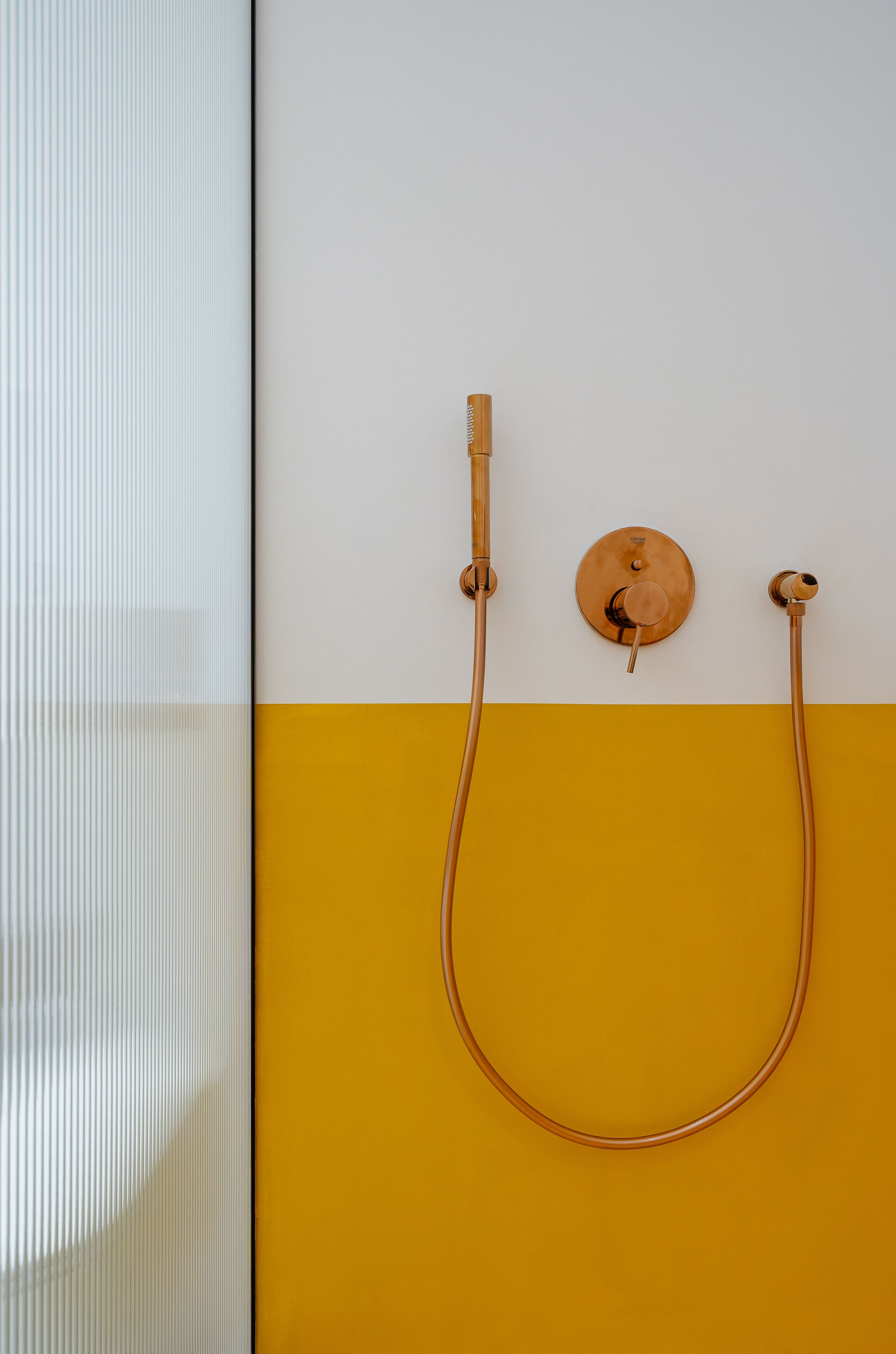 A bathroom with a white and yellow wall, a round sink, and a shower with a curved hose.