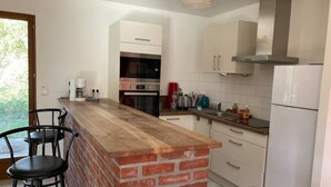 Cocina con isla de ladrillo, armarios blancos, electrodomésticos de acero inoxidable y lámpara colgante.