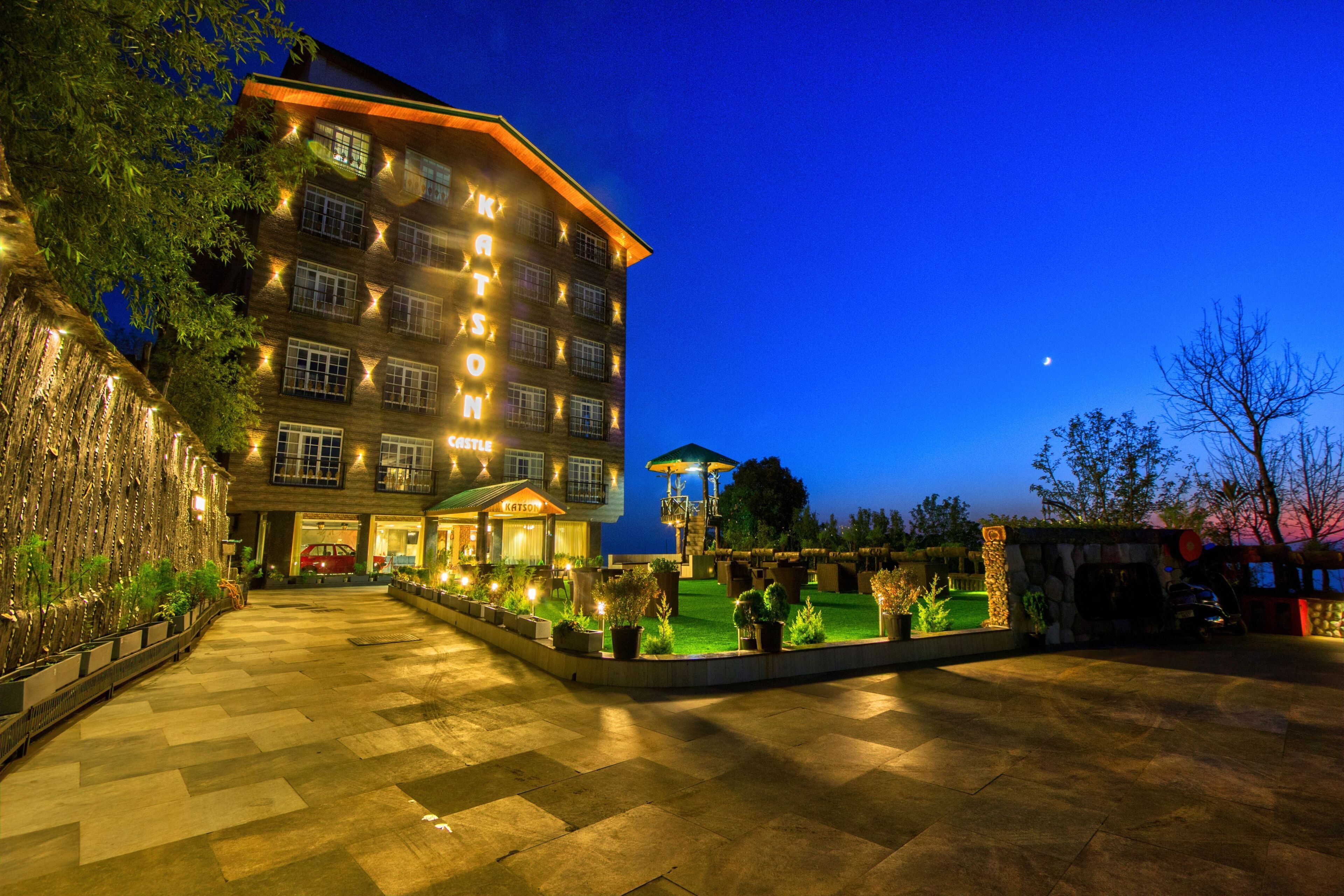 A multi-story hotel with a well-lit entrance, a landscaped courtyard, and a visible swimming pool area.