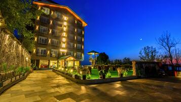 A multi-story hotel with a well-lit entrance, a landscaped courtyard, and a visible swimming pool area.