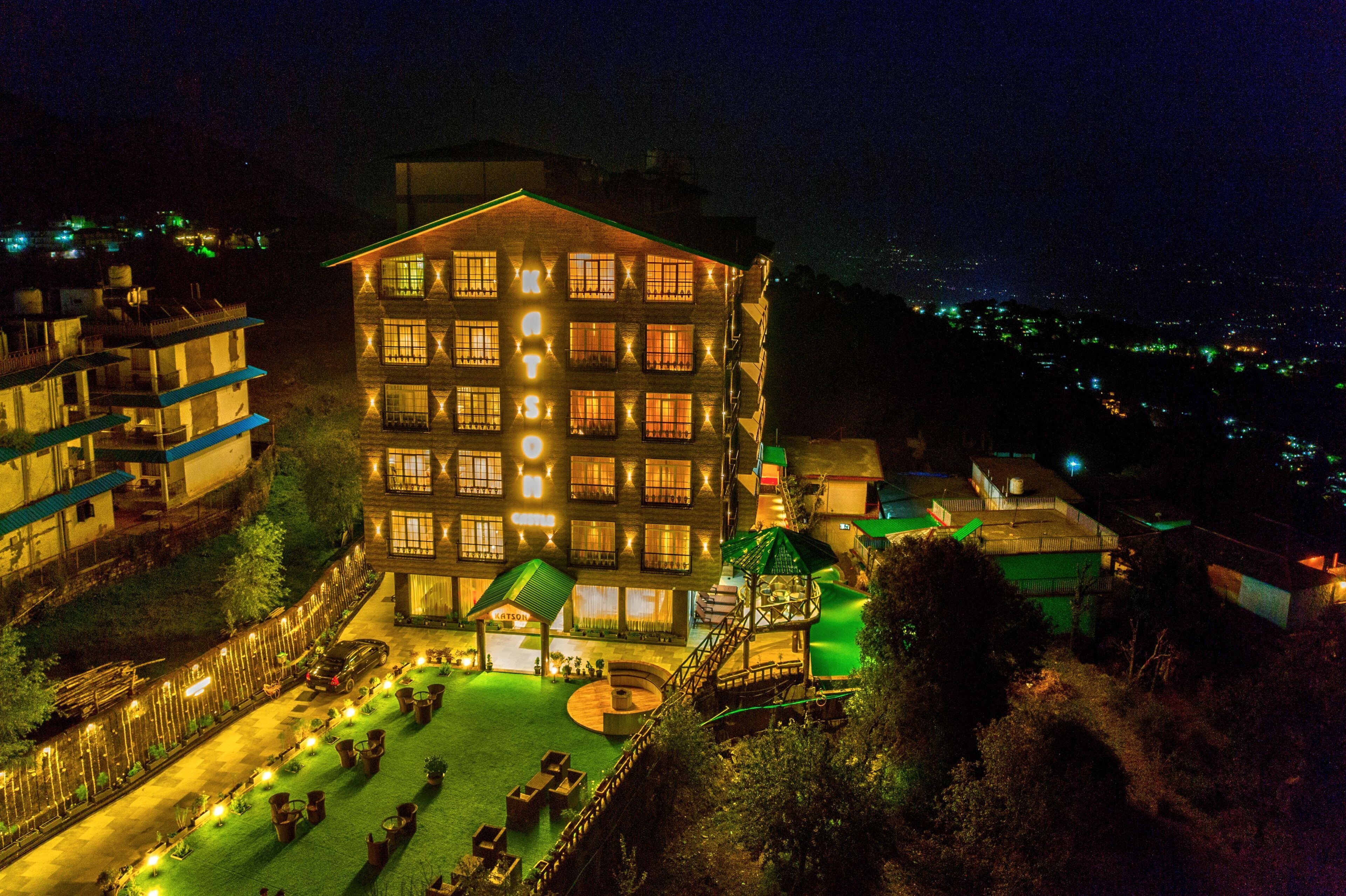 Um hotel com vários andares, fachada bem iluminada, um pátio central com assentos e uma escadaria que leva a um andar superior.