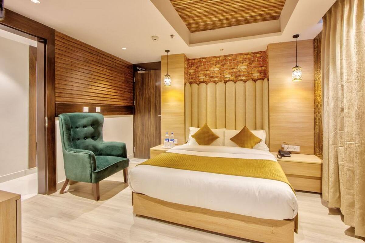 A modern hotel room with a large bed, a green armchair, wooden paneling, and a brick accent wall.