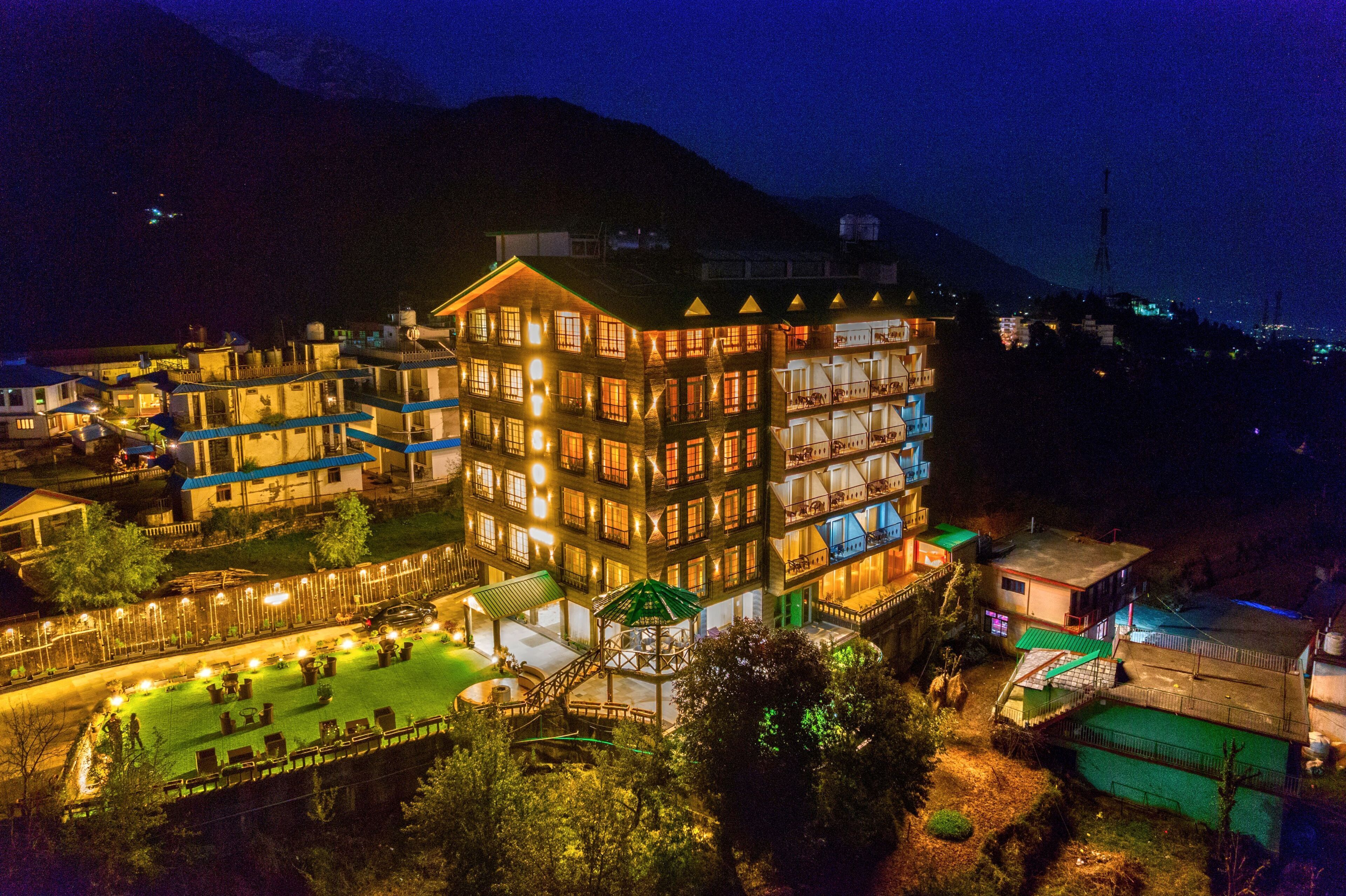 A multi-story hotel with a central courtyard, balconies, and a mountain backdrop.