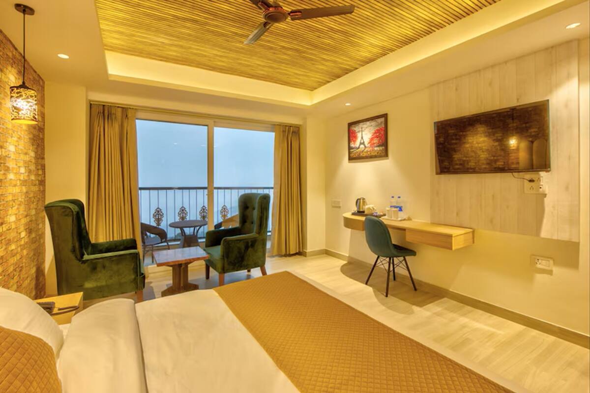 A hotel room with a bed, a desk, a chair, a balcony with a view, and a ceiling fan.