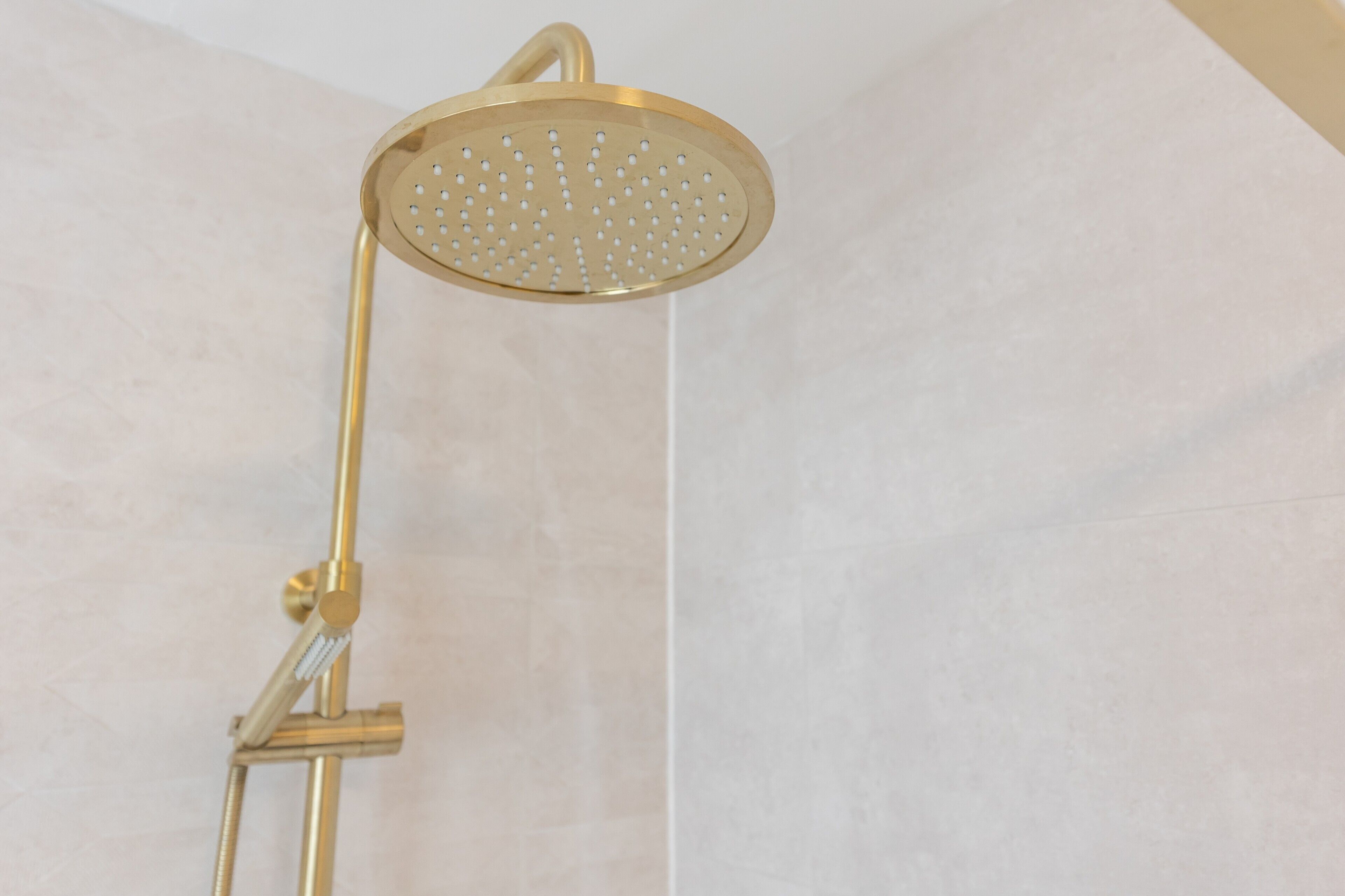 Un pommeau de douche de couleur or, doté d’un flexible, fixé sur un mur avec un drain vertical.