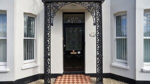 A white building with a black door, a checkered mat, and a black wrought iron gate. - A Stunning Ground Floor Apartment (Reydon)