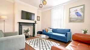 A living room with a fireplace, a blue sofa, a grey armchair, and a coffee table. - A Stunning Ground Floor Apartment (Reydon)