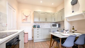 A modern kitchen with white cabinets, a microwave, and a dining area with a table set for two. - A Stunning Ground Floor Apartment (Reydon)