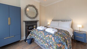 A bedroom with a bed, nightstands, a dresser, a mirror, and a fireplace. - A Stunning Ground Floor Apartment (Reydon)