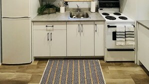 A compact kitchen with wooden ceiling beams, white cabinets, a microwave, a refrigerator, a sink, and a stove. - Riverfront Cottage that offer Incredible views, is pet friendly and private (Tatamagouche)