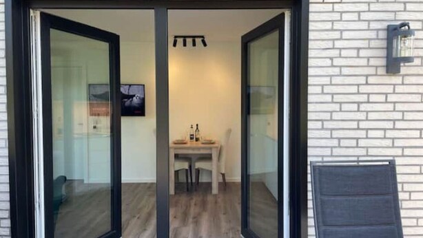 A modern interior with a glass door entrance, a dining area with a table and chairs, and a small seating area with a chair. - Hotel feeling, great location, terrace, BBQ, (Bad Zwischenahn)