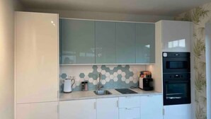 A modern kitchen with white cabinets, a hexagonal tile backsplash, and a built-in oven. - Hotel feeling, great location, terrace, BBQ, (Bad Zwischenahn)