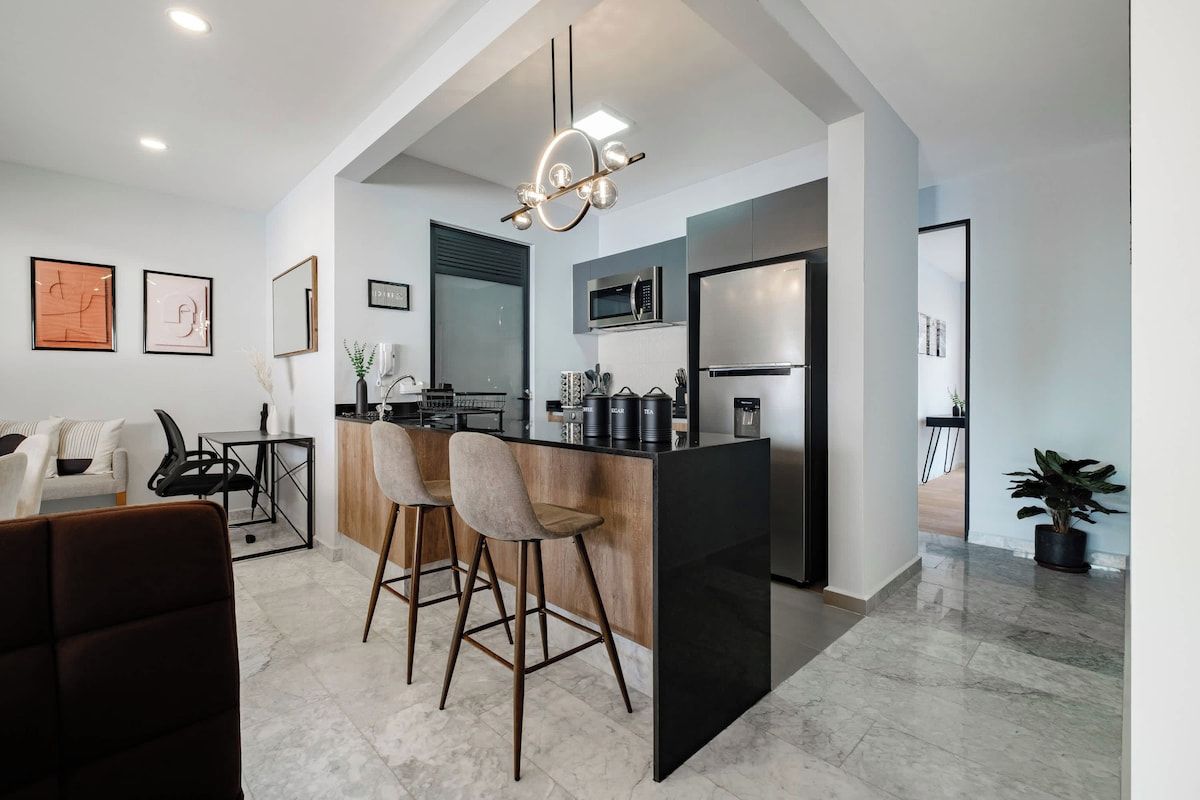 A modern kitchen with a central island, bar stools, a microwave, and a refrigerator.