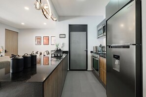 A modern kitchen with a stainless steel refrigerator, a microwave, and a built-in oven. There is a wooden island with black containers and a vase with flowers.