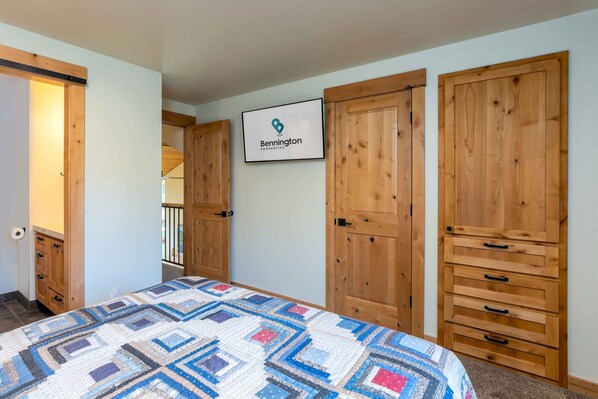 A bedroom with a large bed, wooden wardrobe, and a sign for Bennington Properties. - FAIR06 - Spacious Condo with Pool Views, Hot Tub (Sunriver)