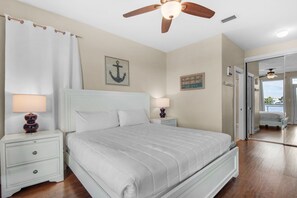 Une chambre à coucher avec un lit, des tables de chevet, un ventilateur de plafond et une vue sur l’extérieur.