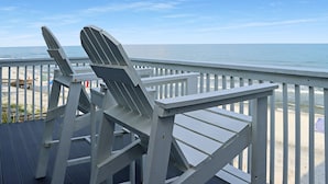 Terraza de madera con sillas Adirondack con vistas a la playa.