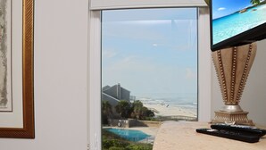 Habitación con ventana grande que da a una playa y piscina, televisión y control remoto sobre la encimera.