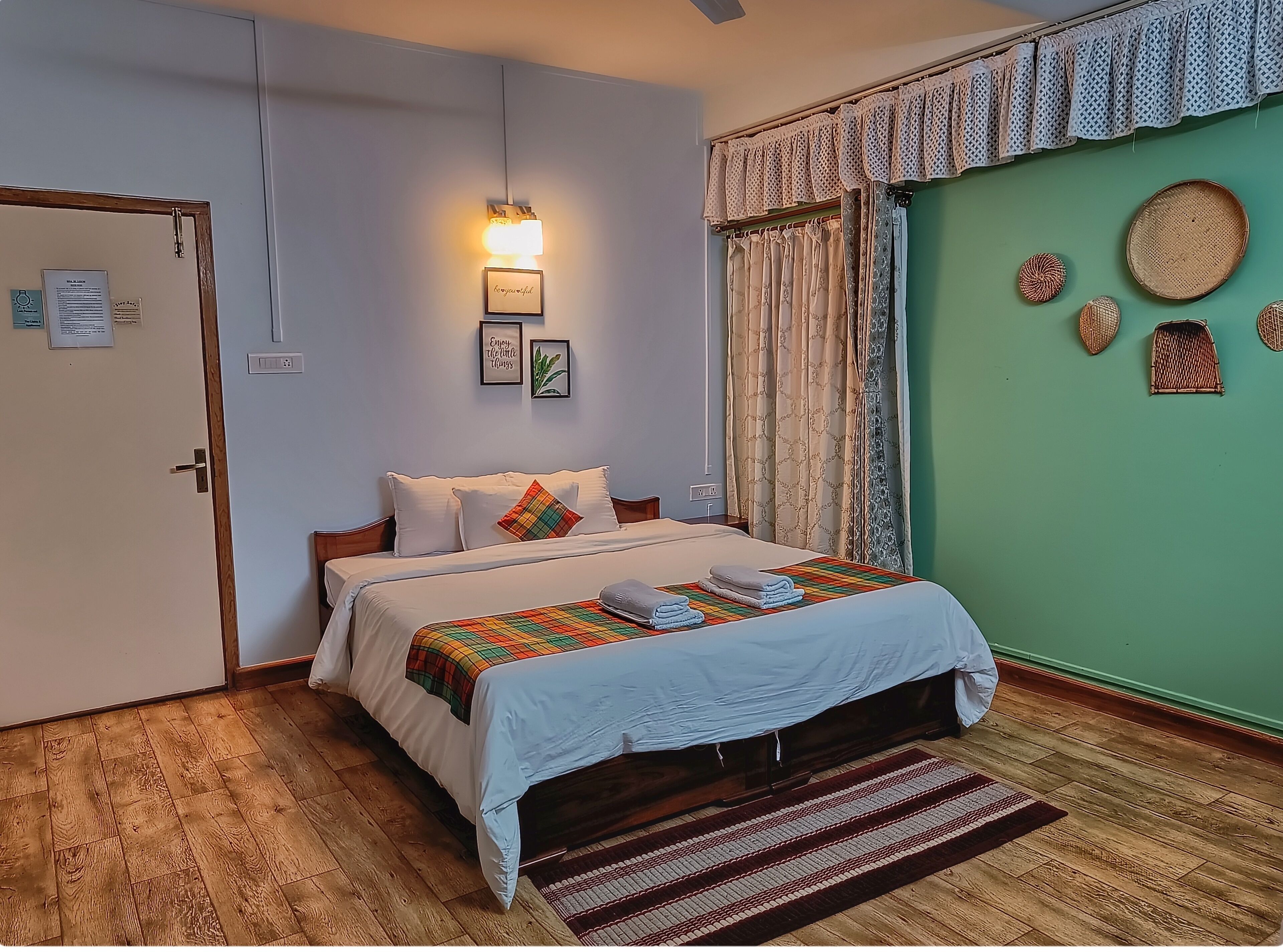 A neatly arranged bedroom with a bed, a bedside lamp, a door, and a green wall with decorative items.