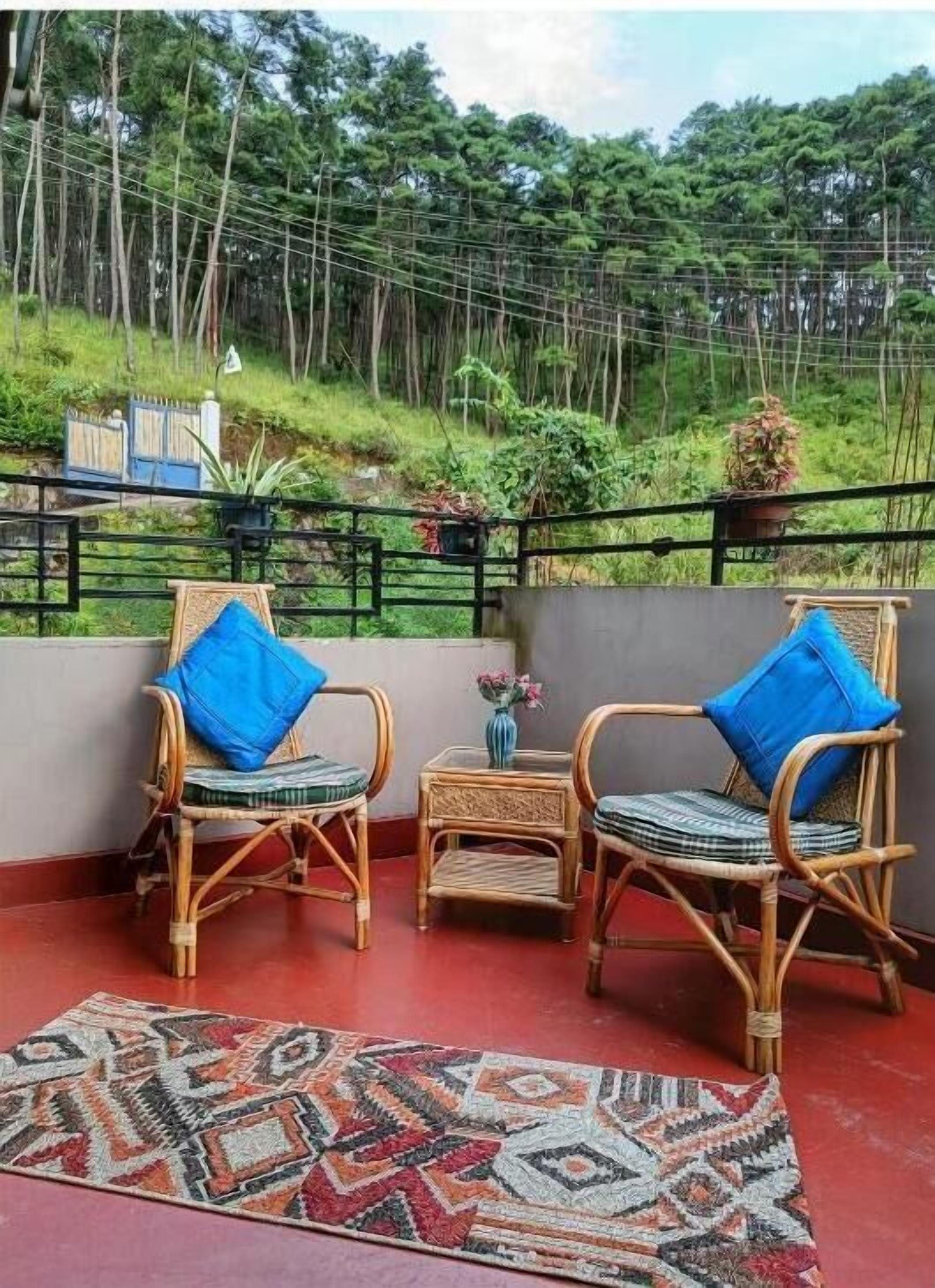 A balcony with wicker furniture and a patterned rug, overlooking a lush green landscape.