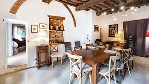 A rustic dining area with a wooden table and chairs, a brick wall, and a chandelier.