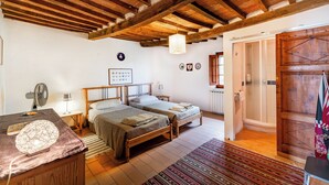 A bedroom with two beds, a wooden ceiling, a fan, a nightstand, a lamp, a rug, and a door with a flag.