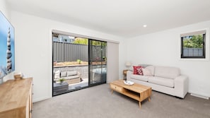 A modern living room with a sofa, coffee table, and a sliding glass door leading to a patio area.