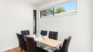 A dining area with a glass table and black chairs, a window with a view of trees, and a door with a sliding glass panel.