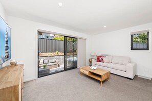 A modern living room with a sofa, a coffee table, and a sliding glass door leading to an outdoor area with a hot tub. - Sandy Views close to Corlette Beach (Corlette)