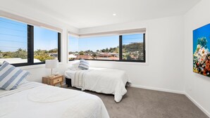 Un dormitorio con dos camas, una mesita de noche, una lámpara y un ventanal con vistas a casas y árboles.