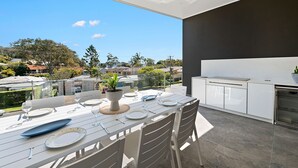 Un área de comedor al aire libre con una mesa para cuatro, una parrilla y vistas del barrio.