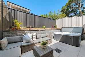 An outdoor patio area with a sofa set, a hot tub, and a stone wall. - Sandy Views close to Corlette Beach (Corlette)