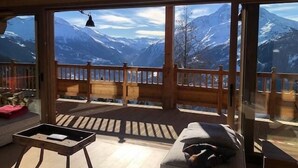 Habitación con un ventanal grande que ofrece vistas a la montaña, una terraza de madera en el exterior y una pequeña mesa con una silla.
