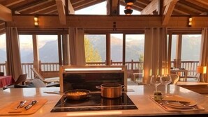 Una cocina con estufa, una sartén y una olla sobre el mostrador. Hay sillas y una mesa con una copa de vino y una botella encima.